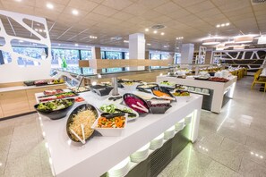 A buffet with various food options, a modern interior design, and large windows. - California Garden (Salou)