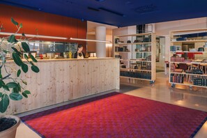 L’intérieur d’une bibliothèque moderne, avec un comptoir d’accueil, des étagères et un espace recouvert d’un tapis rouge.