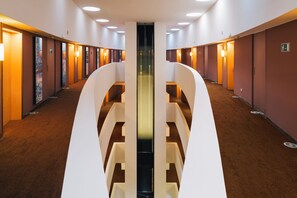 A hotel corridor with a central elevator, multiple doors on either side, and a carpeted floor. - El Sant Cugat (Sant Cugat del Valles)