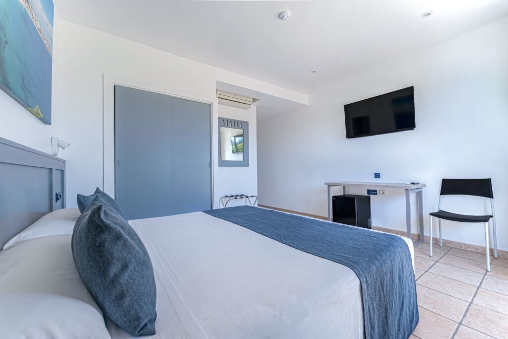 Een hotelkamer met een bed, een bureau, een stoel, een televisie en een deur.