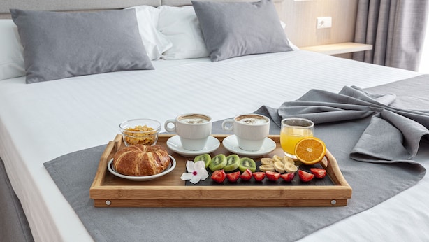A neatly made bed with a tray of breakfast including croissants, fruit, and coffee. - Hospedium Hotel Abril (San Juan de Alicante)