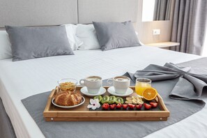 A neatly made bed with a tray of breakfast including croissants, fruit, and coffee. - Hospedium Hotel Abril (San Juan de Alicante)