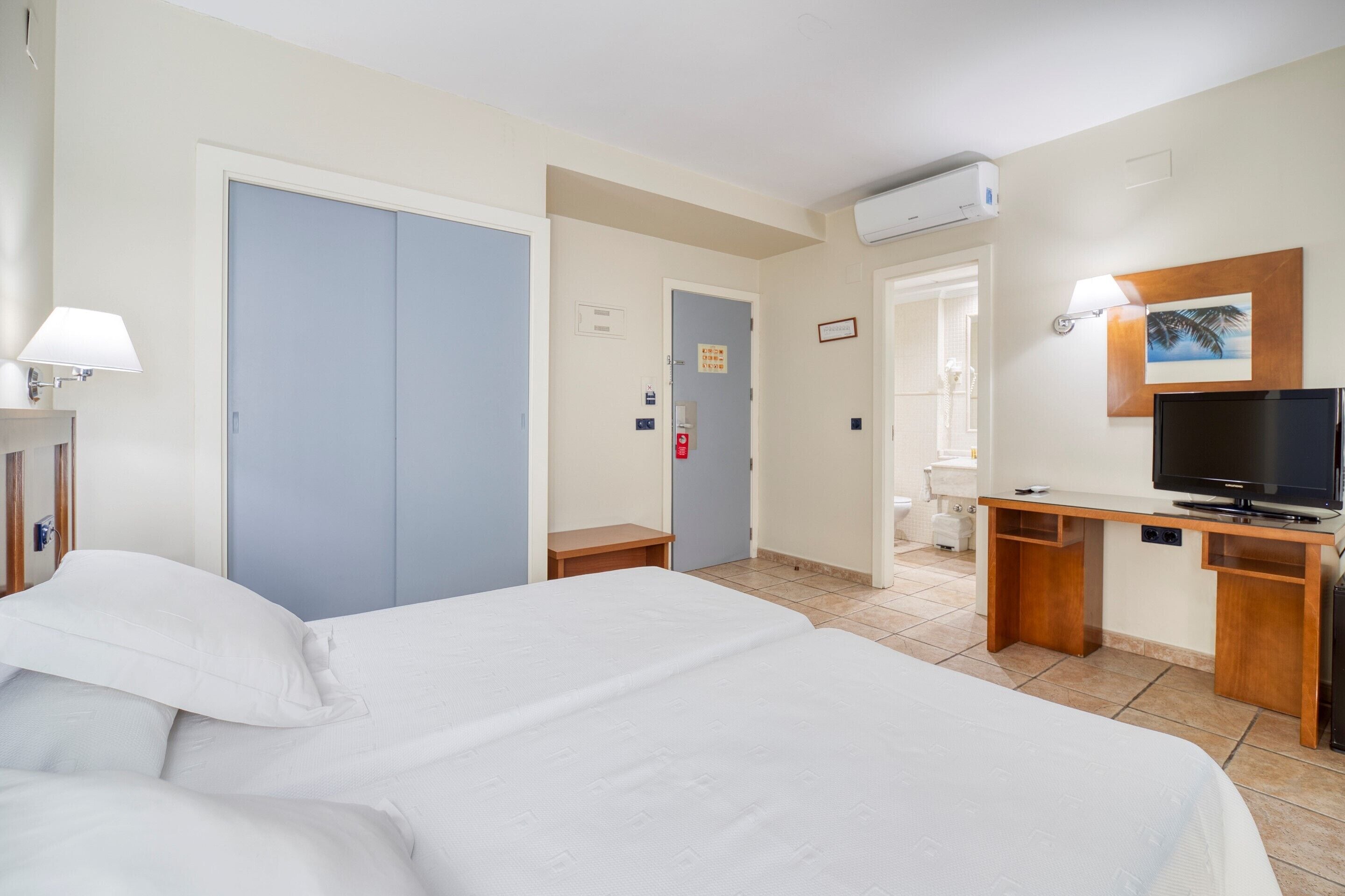 A hotel room with a large bed, a desk with a television, and a bathroom visible through an open door.