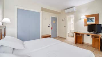 Habitación de hotel con una cama grande, un escritorio con televisor, y un baño visible a través de una puerta abierta.