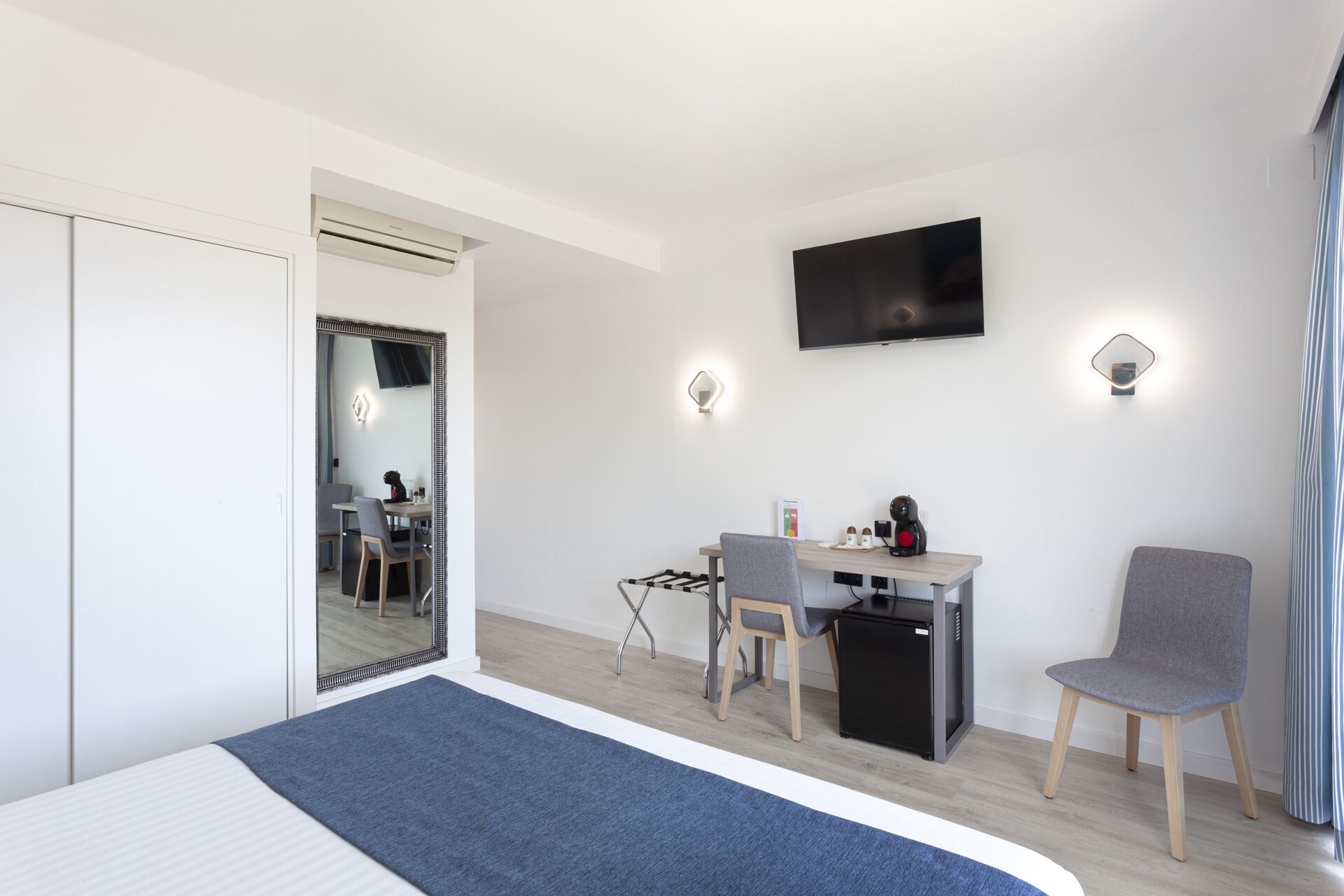 A modern hotel room with a bed, a desk, a chair, a TV, and a mirror.