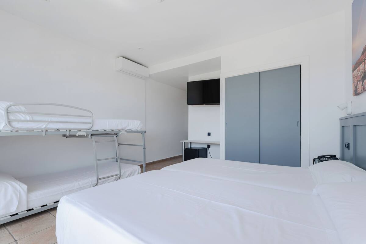 A hotel room with a bunk bed, a desk with a chair, a wardrobe, and a flat-screen TV mounted on the wall.