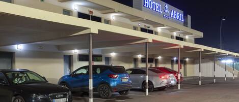 Un hotel con un letrero que dice "HOTEL ABRIL" y varios espacios de estacionamiento con automóviles.