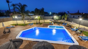 A swimming pool with lounge chairs and umbrellas, surrounded by palm trees and a view of the mountains. - Hospedium Hotel Abril (San Juan de Alicante)
