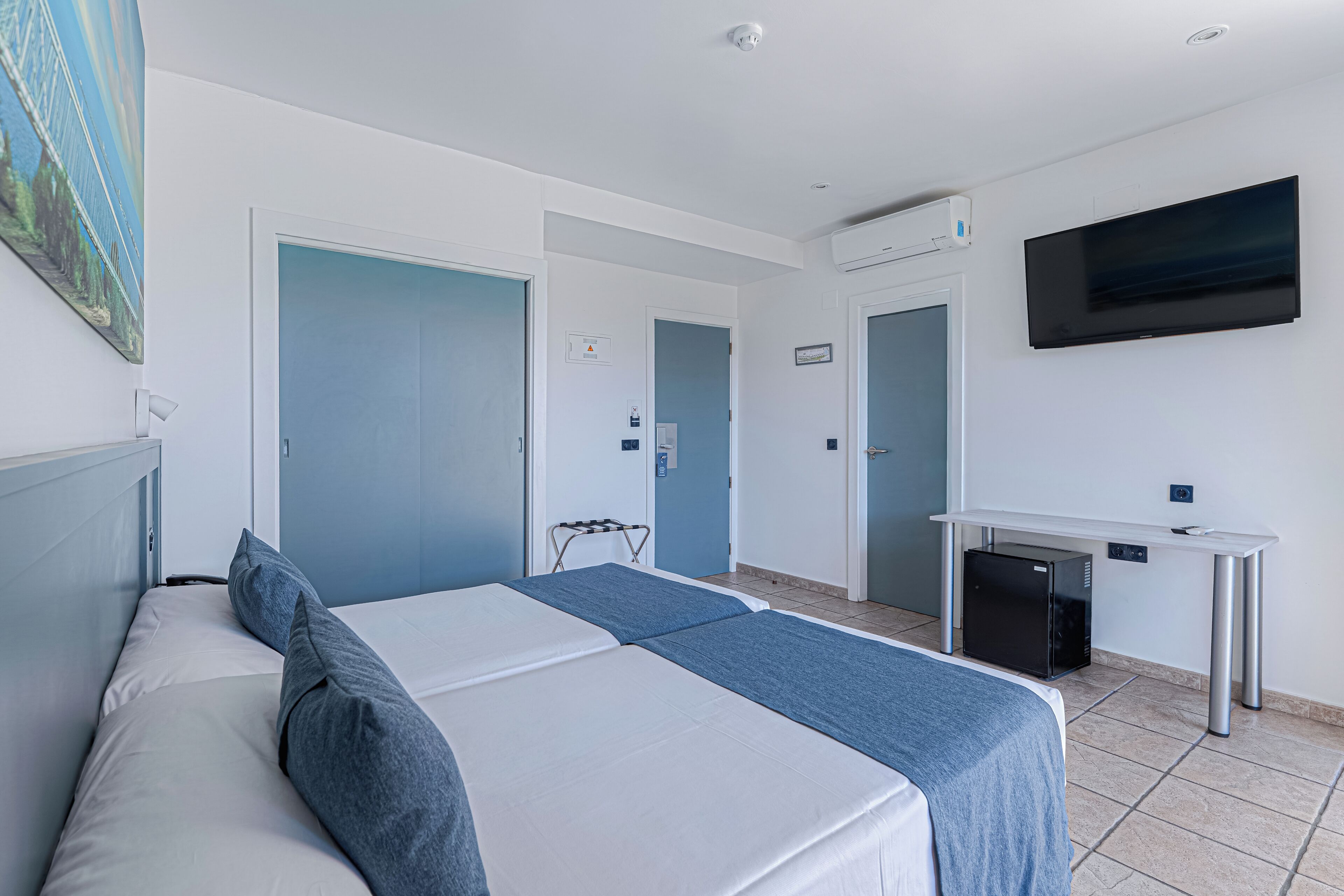 A hotel room with a bed, a desk, a TV, and a small refrigerator.