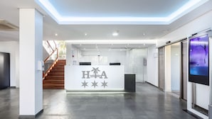 A modern hotel reception area with a central desk displaying the logo 'HHA'. - Hospedium Hotel Abril (San Juan de Alicante)