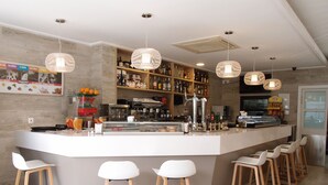 A modern bar area with a central counter, multiple stools, hanging pendant lights, and a variety of bottles and snacks on shelves. - Hospedium Hotel Abril (San Juan de Alicante)