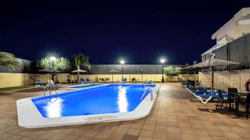 Piscina con sillas de descanso y sombrillas, rodeada por un patio con baldosas.