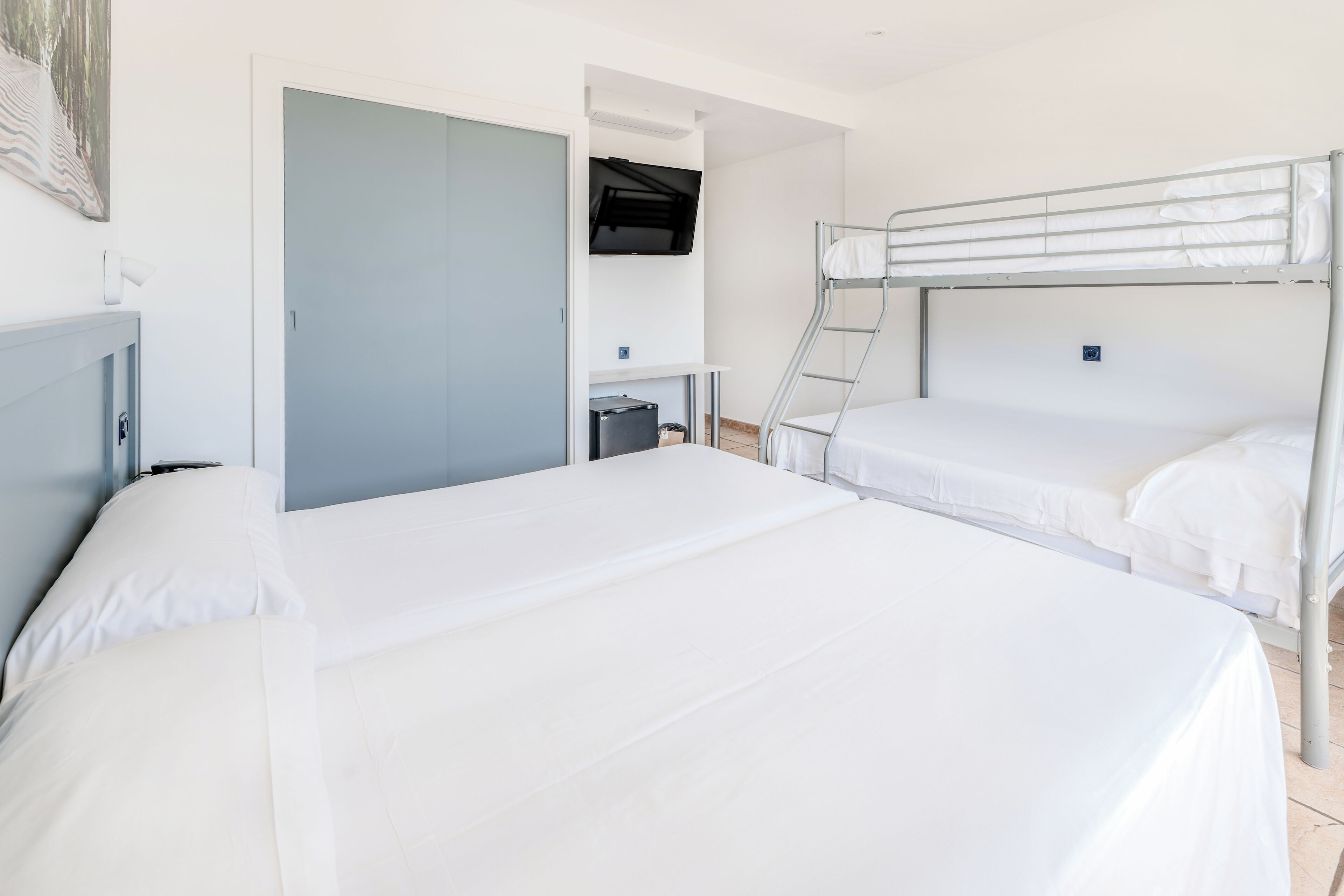 Habitación de hotel con literas, un escritorio con silla, un televisor montado en la pared y un armario.