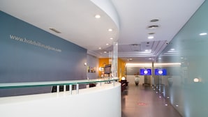 A reception area with a glass railing, a reception desk, and a wall with a website address. - Hotel Villa San Juan (San Juan de Alicante)