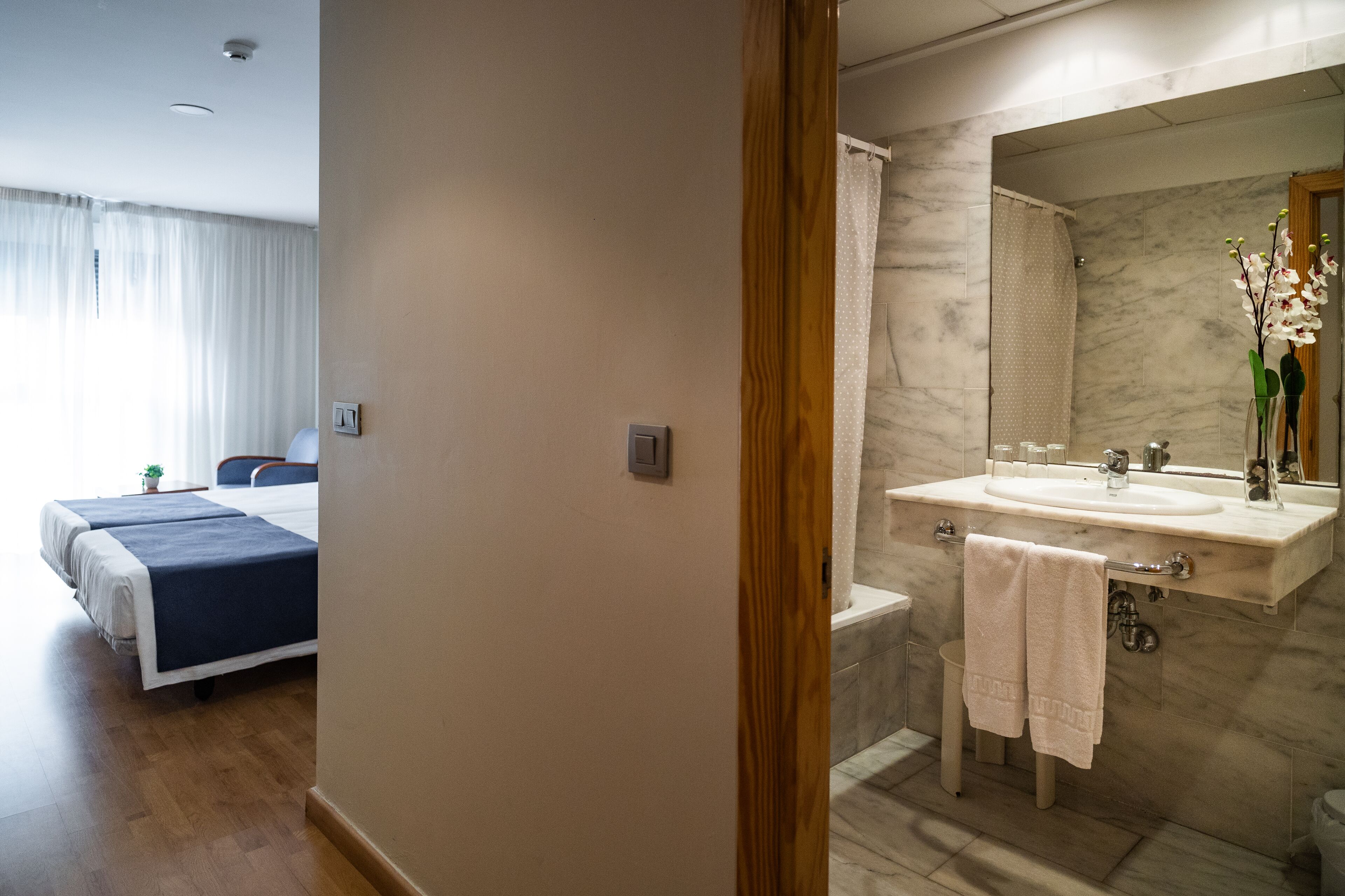 A hotel room with a bed, a bathroom with a sink and mirror, and a shower.