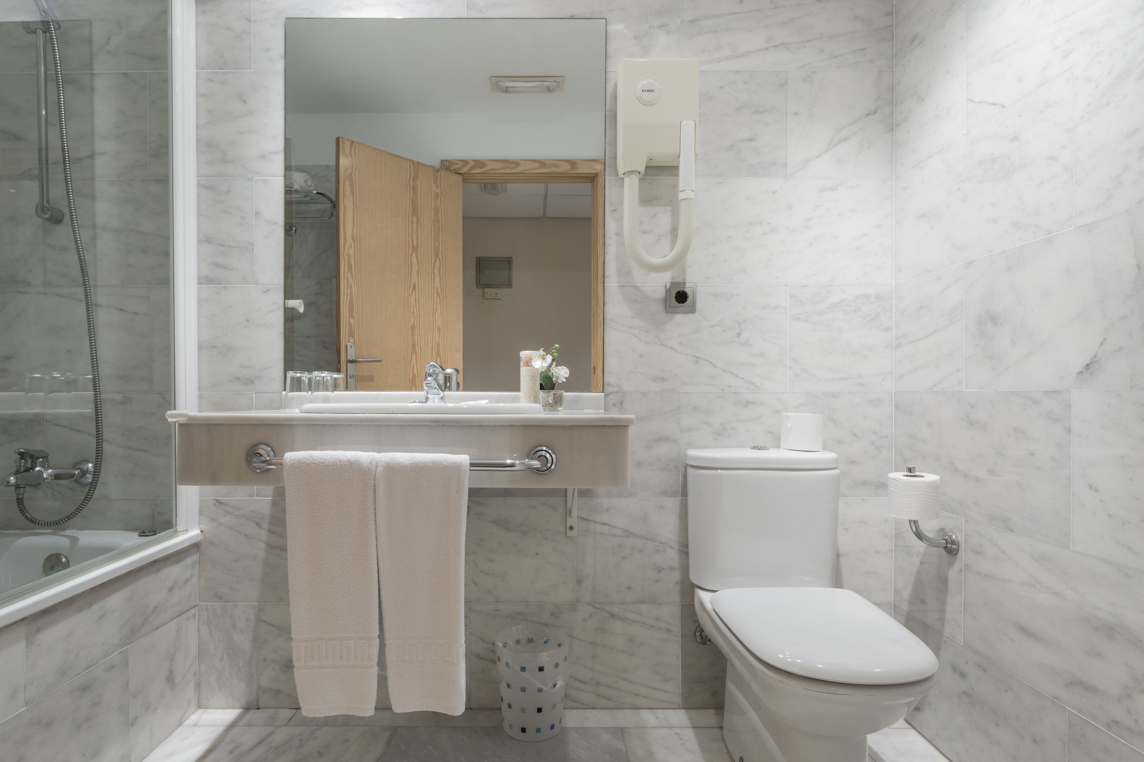 A modern bathroom with a marble floor, a glass-enclosed shower, a toilet, and a sink with a mirror above it.