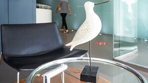 A modern interior with a glass table holding a white bird sculpture, a black chair, and a person walking in the background. - Hotel Villa San Juan (San Juan de Alicante)