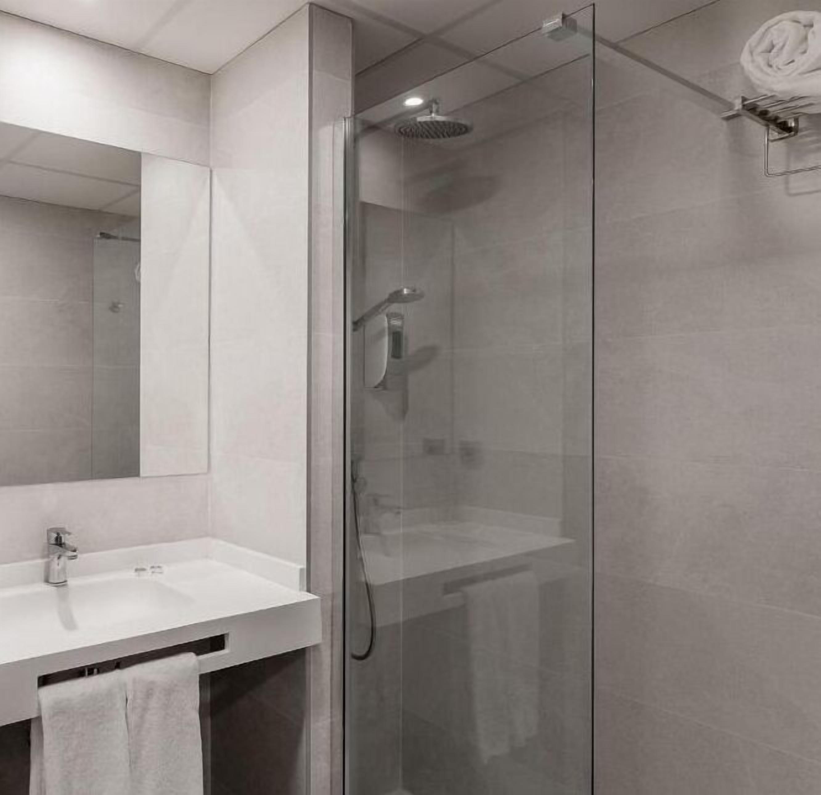 Un baño moderno con ducha de vidrio, lavamanos blanco y un espejo grande.