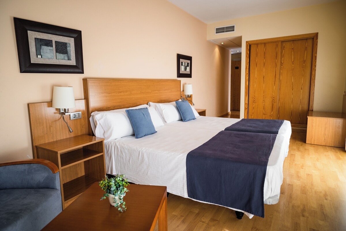 A hotel room with a bed, bedside tables, a desk, and a chair.