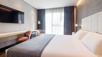 Quarto de hotel moderno com uma cama grande, televisão de tela plana na parede, escrivaninha com cadeira e janela com cortinas.