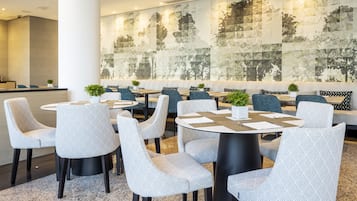 Un comedor moderno con mesas redondas, sillas estampadas y un gran mural abstracto en la pared.