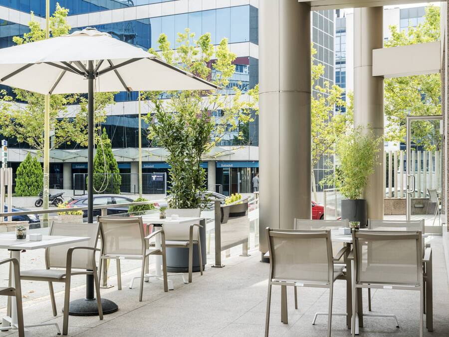An outdoor seating area with tables and chairs, large umbrellas, and potted plants.