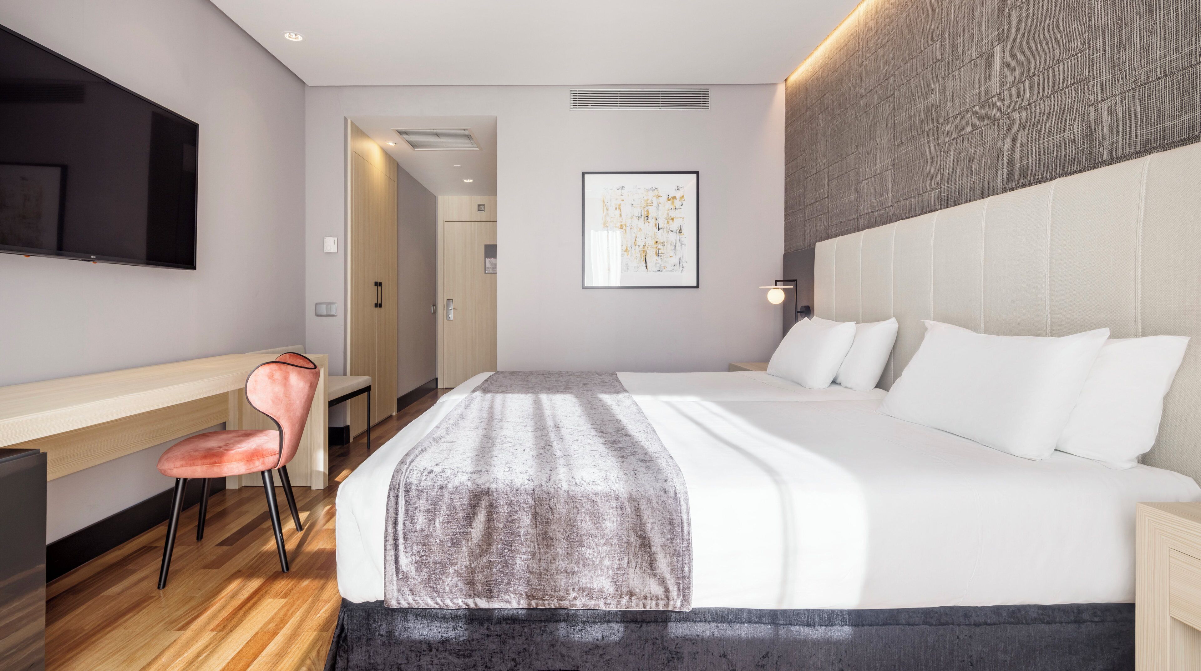 Una habitación de hotel moderna con una cama grande, un escritorio, una silla y un televisor de pantalla plana.