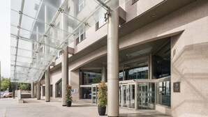 A modern building with a glass entrance, large pillars, and potted plants. - Hotel ILUNION Alcalá Norte (Madrid)