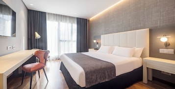 A modern hotel room with a large bed, a desk, and a chair.