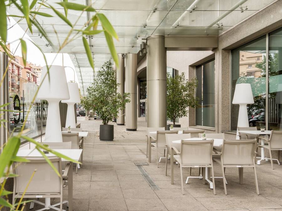 An outdoor cafe area with tables and chairs, potted plants, and a glass ceiling.