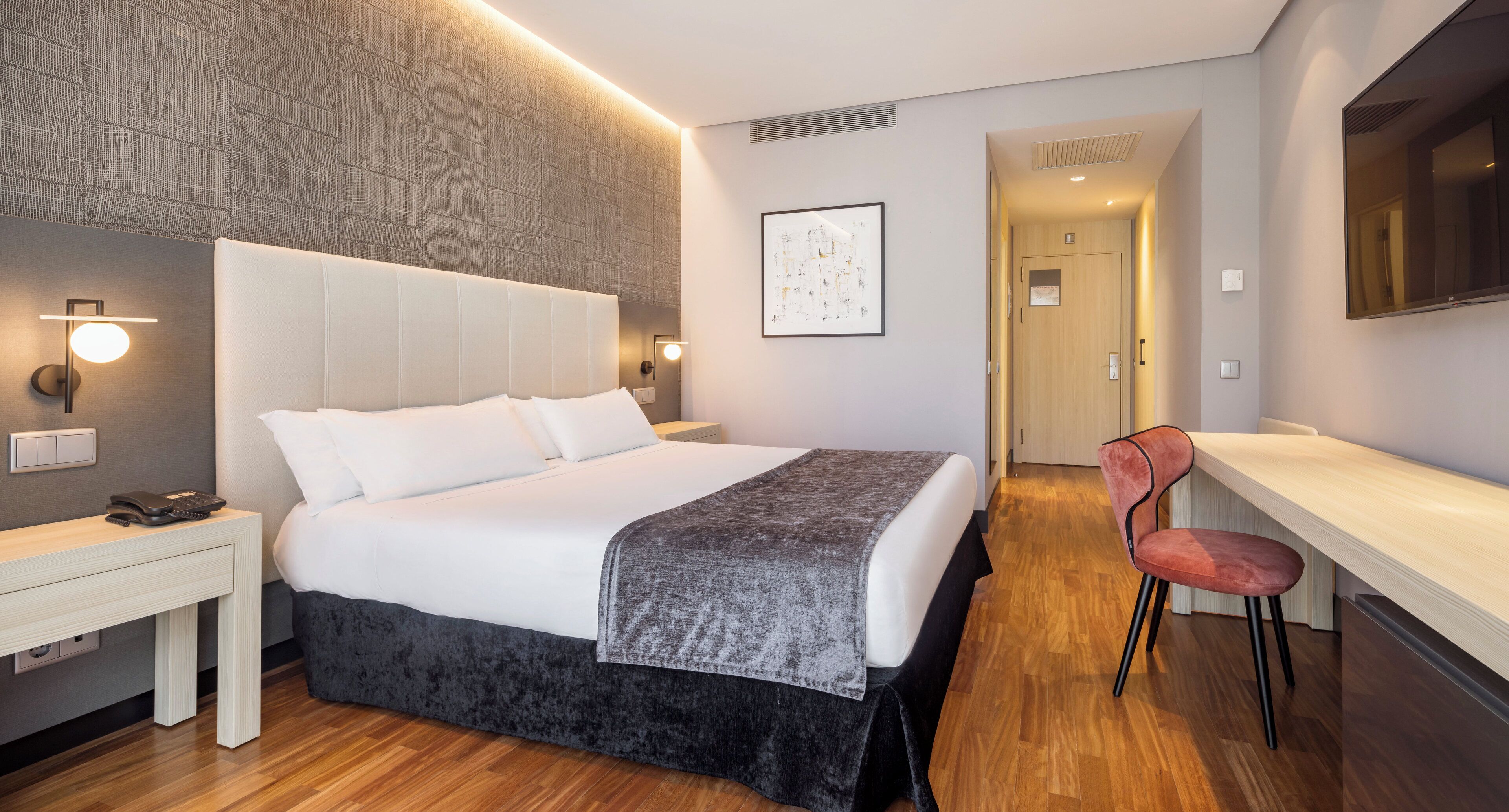 Una habitación de hotel moderna con una cama grande, una mesita de noche y un escritorio con una silla.