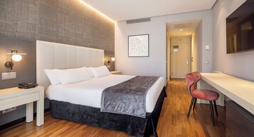 Una habitación de hotel moderna con una cama grande, una mesita de noche y un escritorio con una silla.