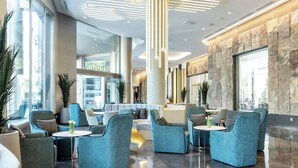 A modern lobby with seating areas, a reception desk, and a stone accent wall. - Hotel ILUNION Alcalá Norte (Madrid)