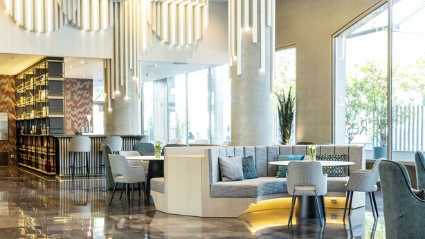 A modern lobby with a seating area, a bar, and large windows. - Hotel ILUNION Alcalá Norte (Madrid)