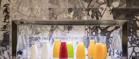 Una estación de bebidas con diversas opciones en recipientes de vidrio, frente a una pared con diseño de hojas.