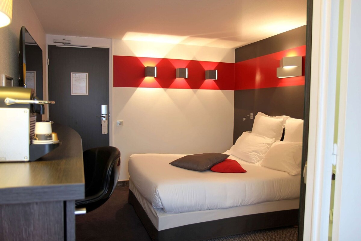 A hotel room with a bed, a desk, and a chair.