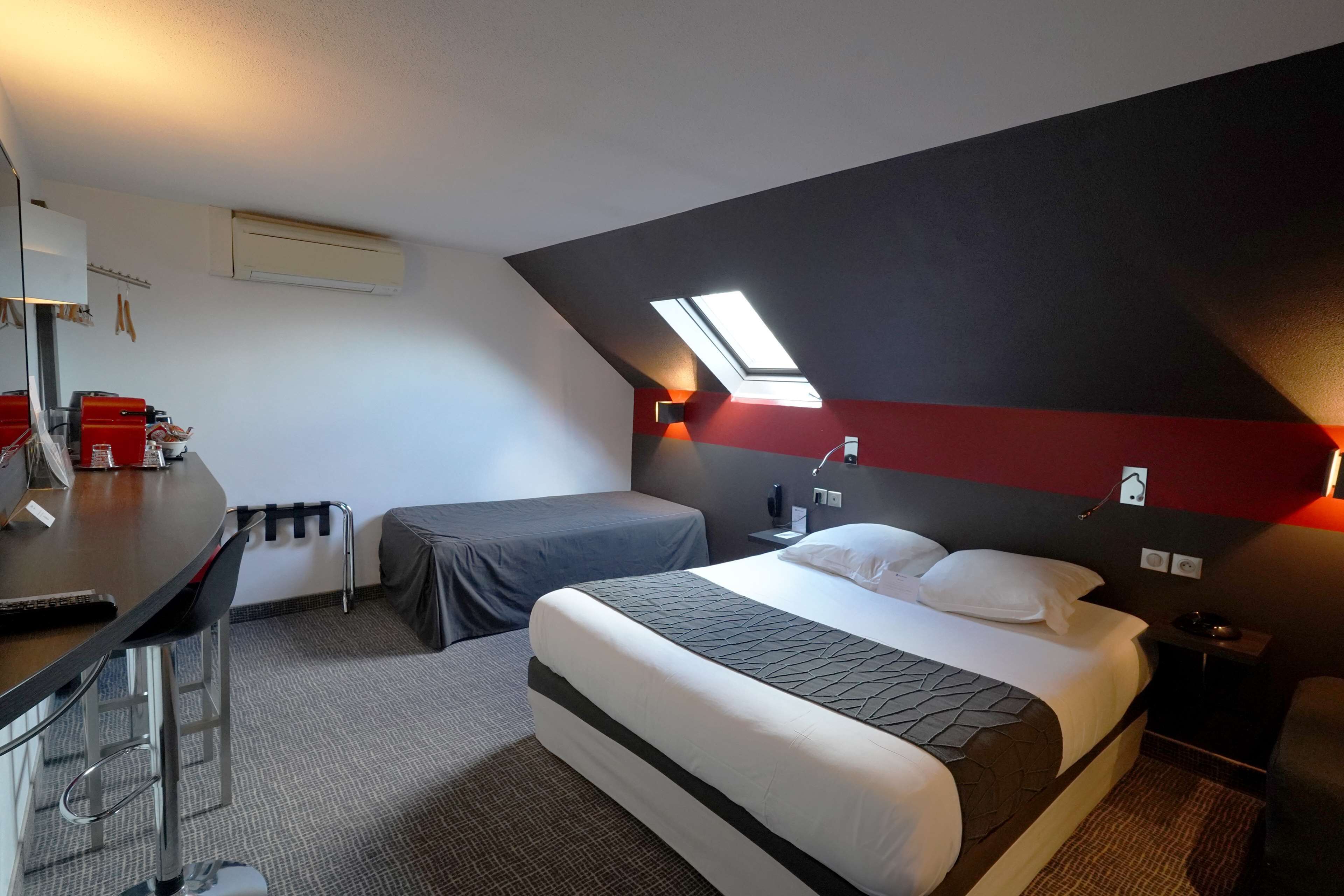 Une chambre d’hôtel comprenant un lit, un bureau, une chaise, une petite table, une table de chevet et une lampe.