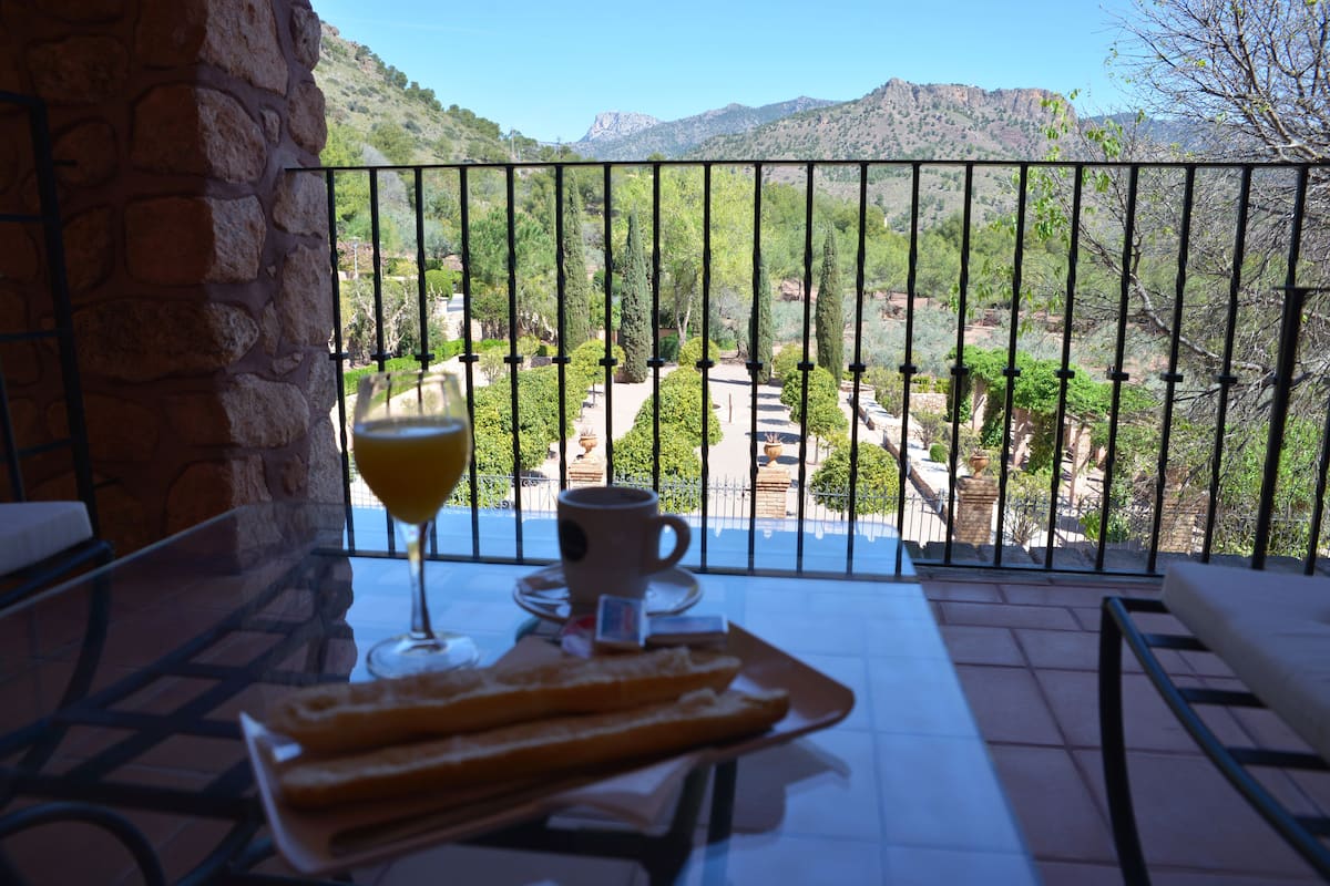 Een balkon met een ontbijttafel, een glas sinaasappelsap en een kop koffie.