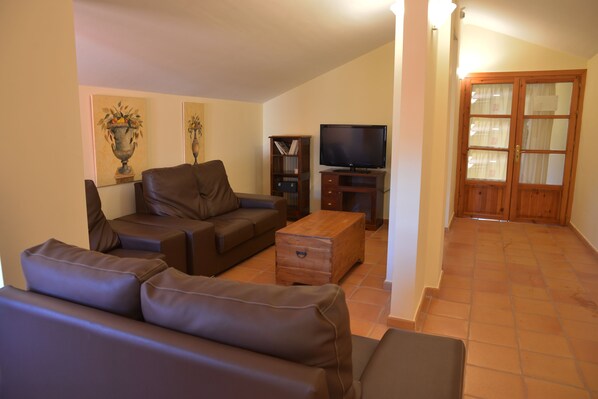 A living room with a brown leather sofa, a wooden coffee table, a television, and a bookshelf.
