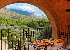 A balcony with a table set for breakfast overlooking a mountainous landscape.