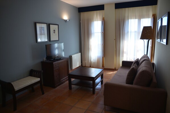 A living room with a sofa, a small table, a bench, a TV, and a lamp.