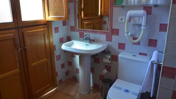 A bathroom with a sink, mirror, toilet, and a trash bin.