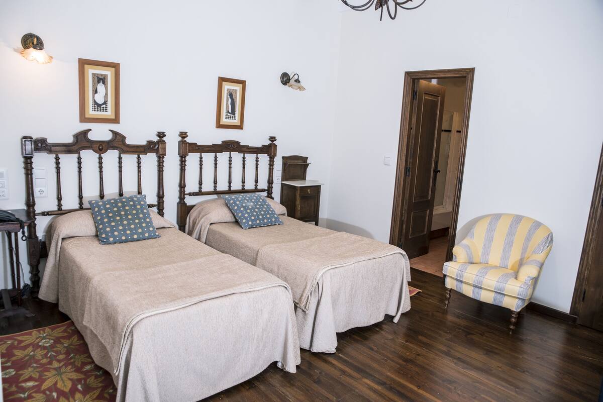 A room with two single beds, a wooden chair, and a door leading to another room.