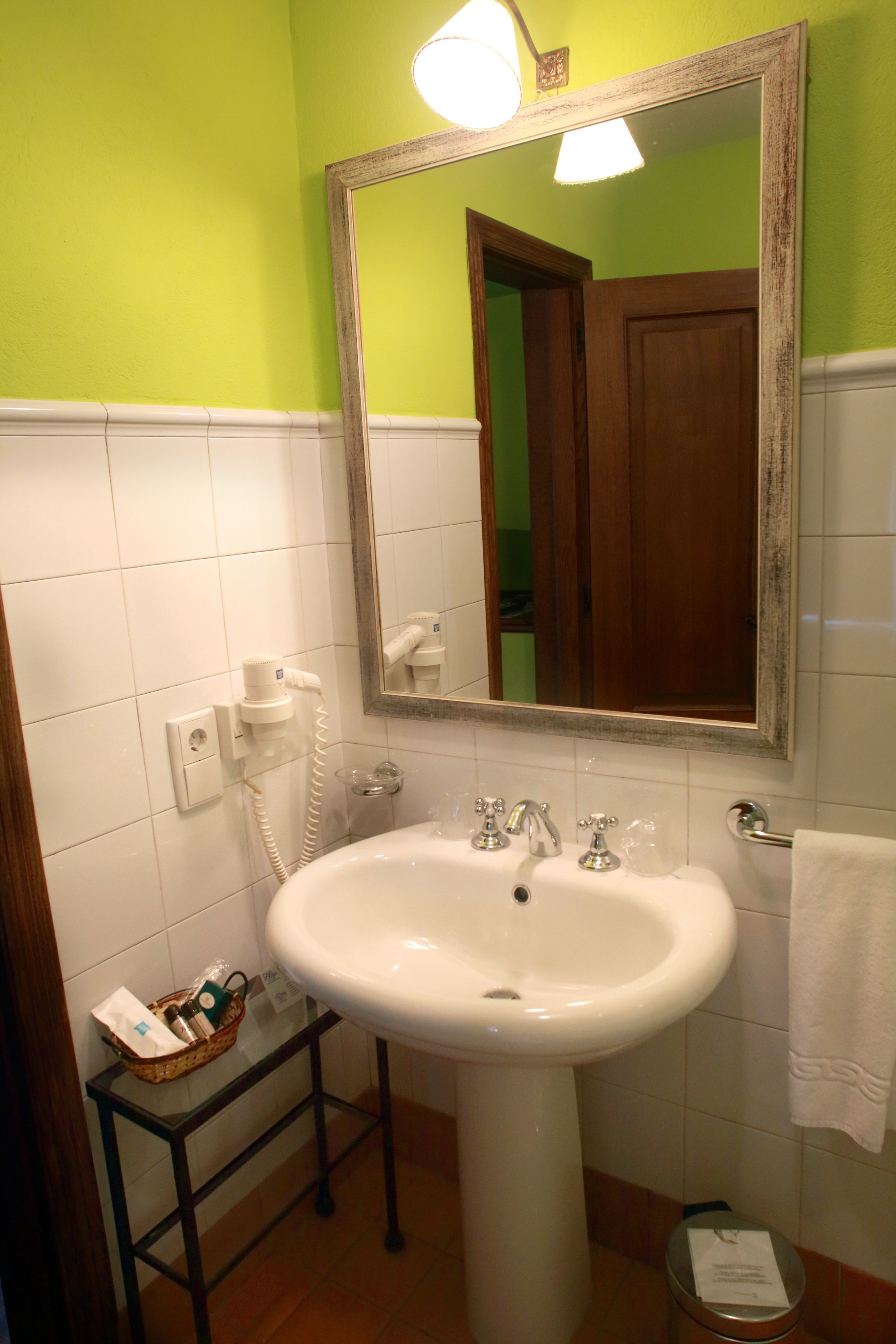 Une salle de bain avec un lavabo blanc, un miroir, un sèche-cheveux et un panier contenant des articles de toilette.