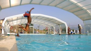 Une piscine intérieure dotée d’un toit en verre, avec une eau cristalline, où l’on peut voir des gens nager et sauter.