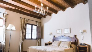 Une chambre à coucher avec un plafond en bois, un lit avec une tête de lit, deux tables de chevet, une lampe de sol et des rideaux.