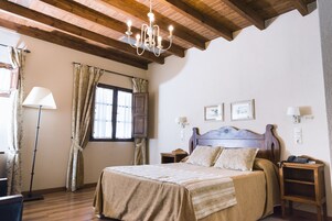 Un dormitorio con techo de madera, una cama con cabecera, dos mesitas de noche, una lámpara de pie y cortinas.