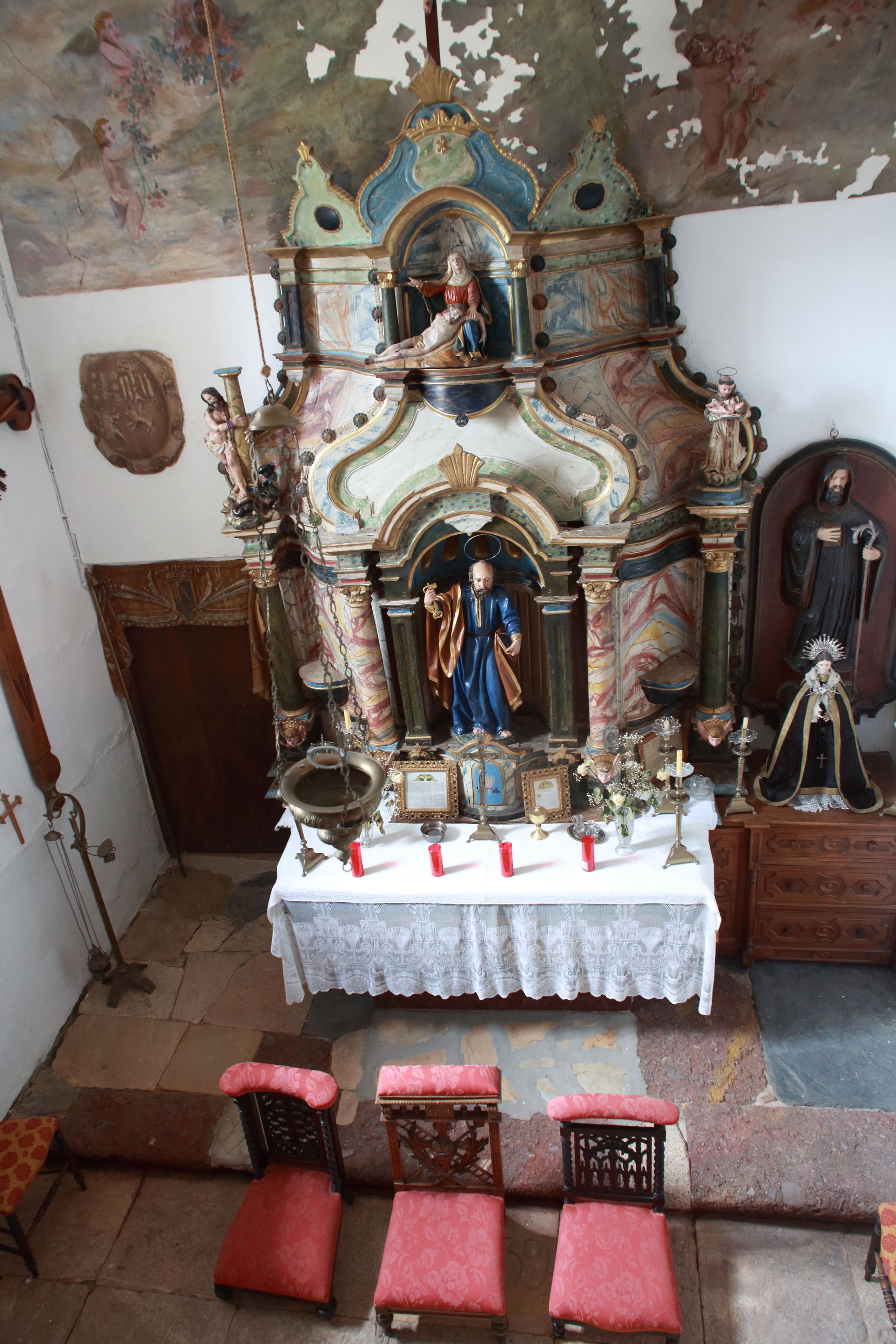 Un santuario religioso ornamentado con una estatua de un santo, un crucifijo y un icono religioso enmarcado.