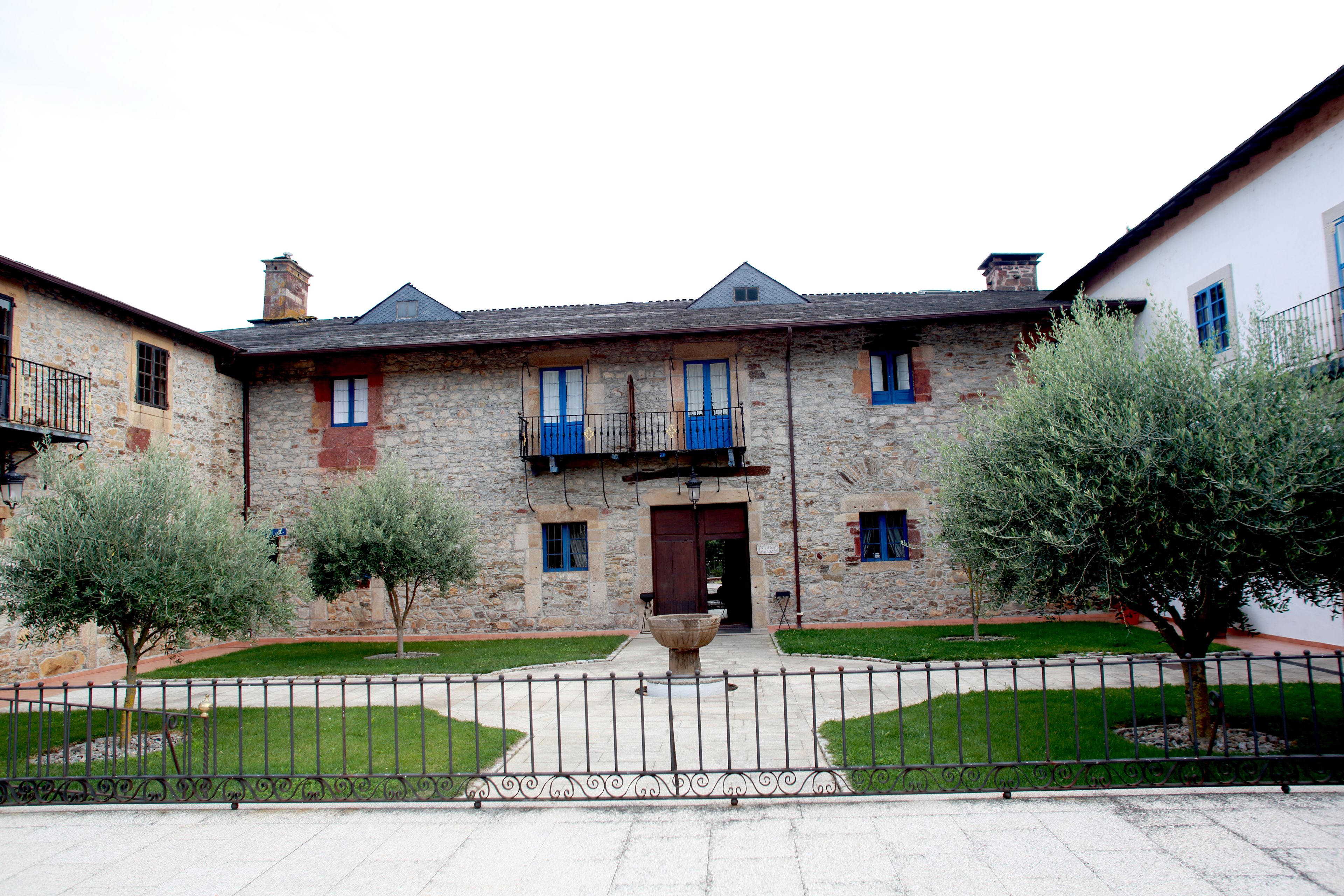 A stone building with a central entrance, a small balcony, and a surrounding fence.