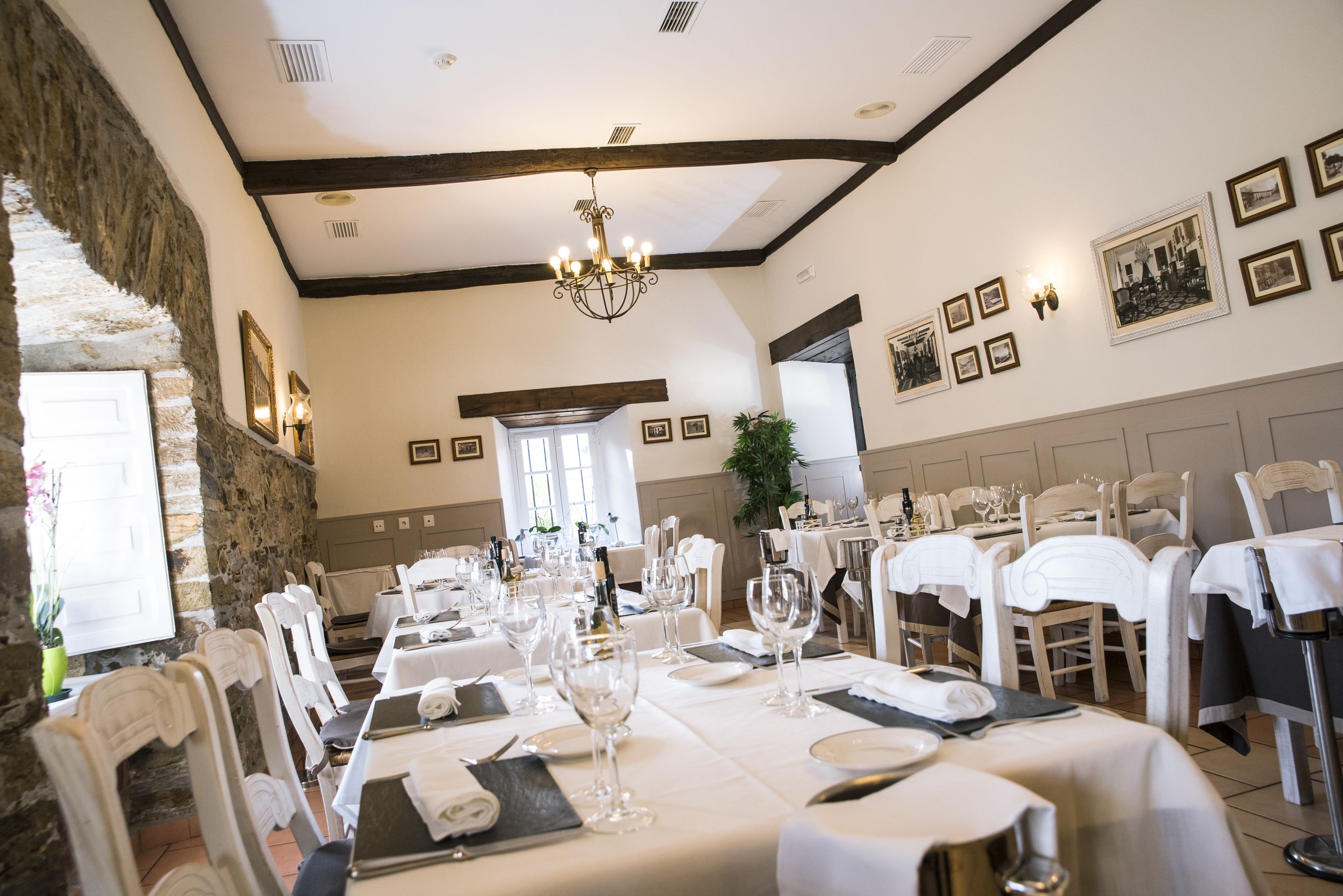 A formal dining room with white tablecloths, neatly set tables, and a chandelier.